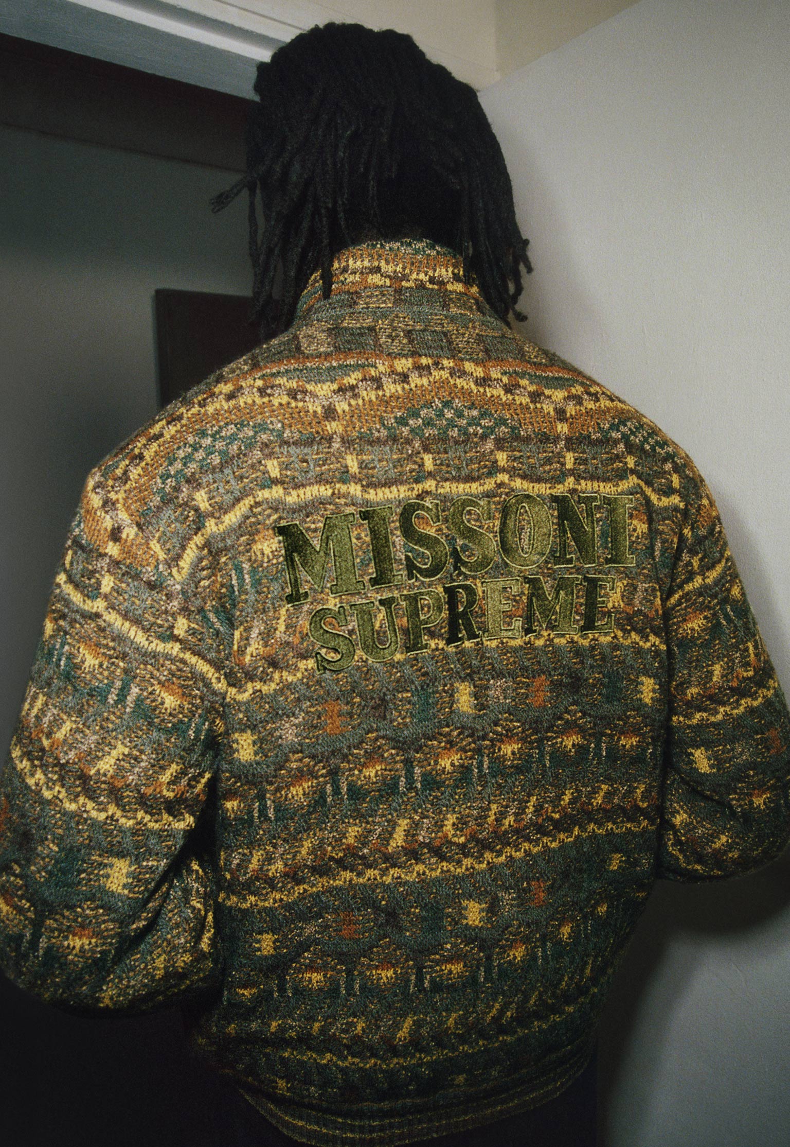 The model who is seen from the back is wearing a green jacket with interesting motifs