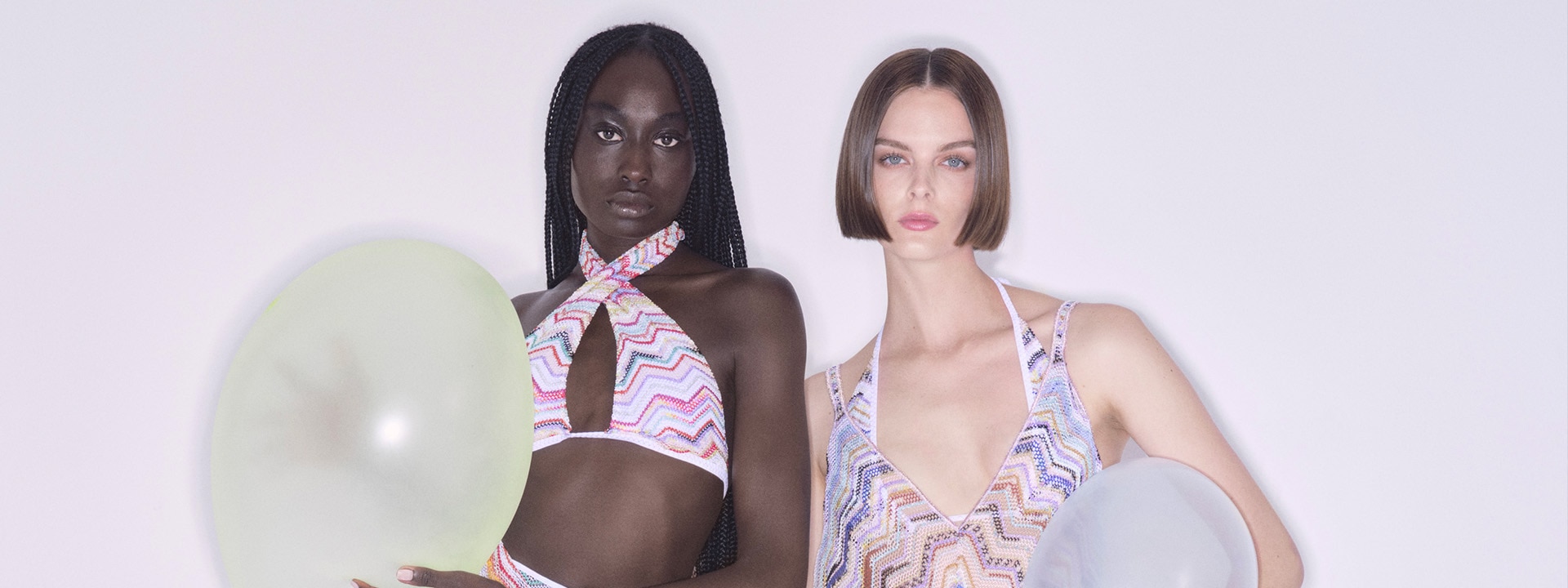 Two models are wearing outfits from the beachwear collection: both are in multicoloured zig zag. The model on the left is wearing a pink bikini and a long skirt, while the model on the right is wearing a dress