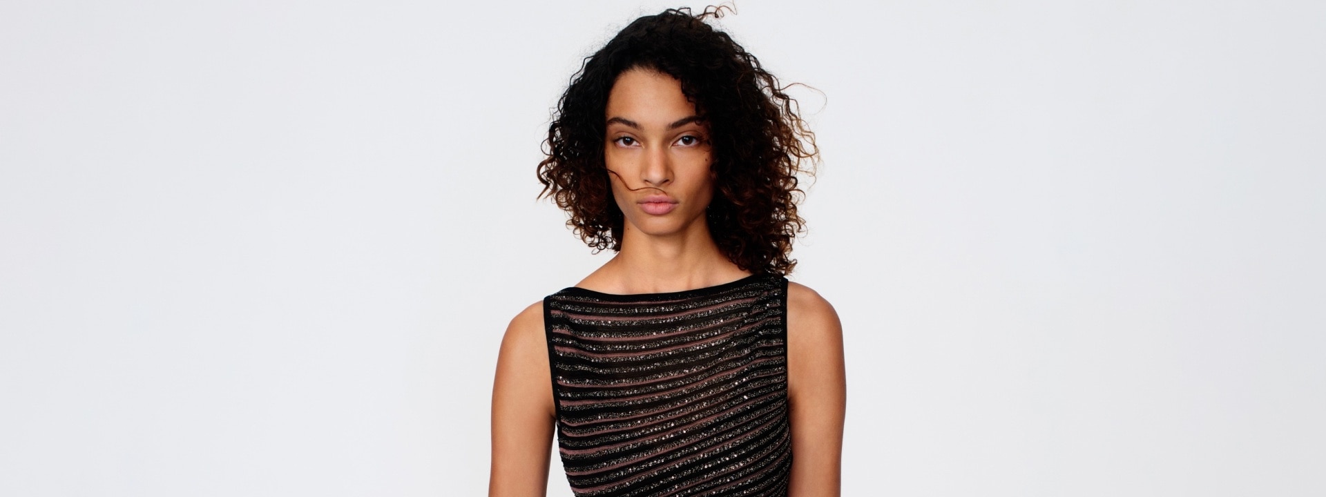 A model is wearing a sleeveless dress with black and sheer horizontal striped pattern.
