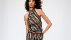 A model is wearing a two pieces jumpsuits, with a sleeveless top and a pair of long trousers, in brown striped tones
