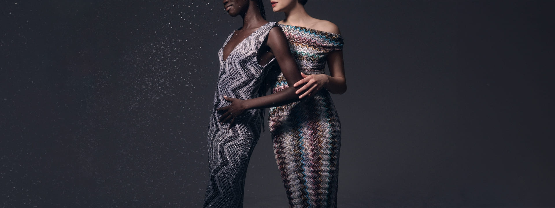 Two models are wearing two dresses from the Fall Winter collection, both sleeveless and with zig zag patterns, in the shade of silver