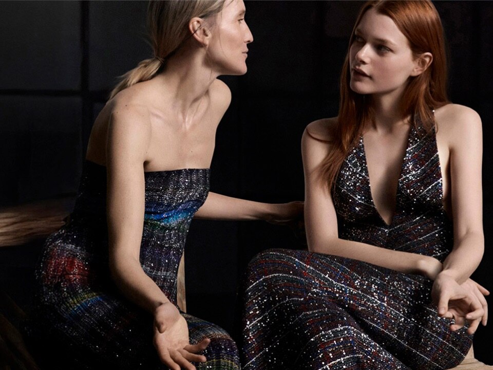 A model is wearing a long sleeveless dress with black, silver, and beige sequined striped pattern.